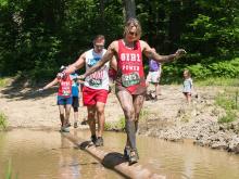 Participants balancing on a log at Holiday Valley's Mudslide mud run event